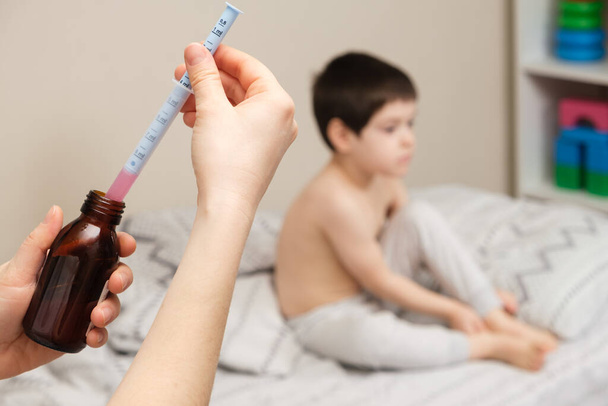 El pediatra o la madre escriben en una jeringa dosificadora el medicamento para la tos o el jarabe de temperatura para el niño.. - Foto, Imagen