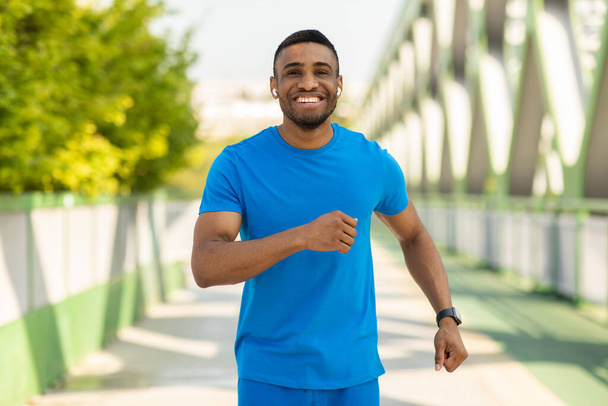 Portrait of an athletic young man running outdoors on a bridge. High quality photo - Zdjęcie, obraz