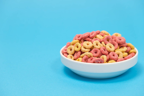 Colazione rapida di cereali nella forma di anelli su un piatto su uno sfondo azzurro. - Foto, immagini