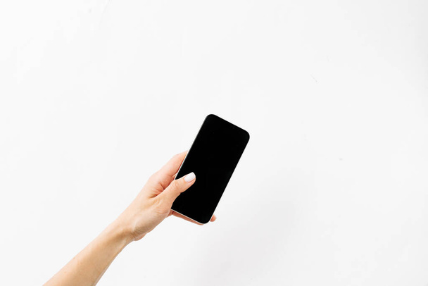 female hand holding a black smartphone on white background - Zdjęcie, obraz