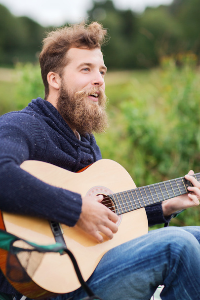 smiling man playing guitar in camping - Zdjęcie, obraz