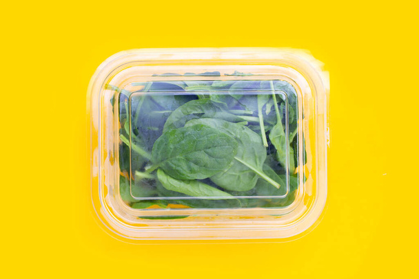 Spinach leaves in plastic box on yellow background. - Photo, Image