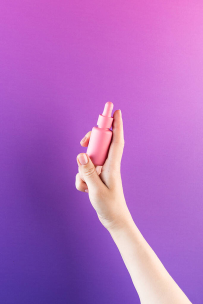 A mock-up of a pink dropper with skin oil in a womans hand on a purple background. - Foto, Bild