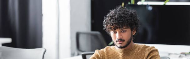 young and curly indian man working in advertising agency, banner - Foto, afbeelding