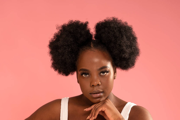 Beauty portrait of young african woman with clean healthy skin, natural makeup and fashionable hairstyle. Girl looking at the camera, posing on pastel pink studio background.  - 写真・画像