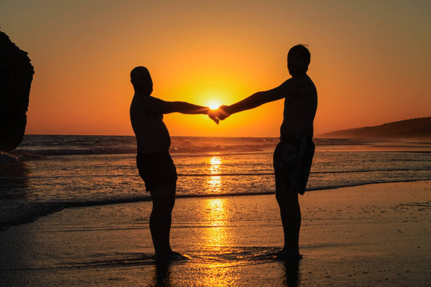 ένα γκέι ζευγάρι ποζάρει στην παραλία το ηλιοβασίλεμα - Φωτογραφία, εικόνα