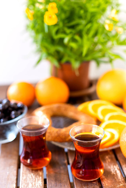 Türk kahvaltısı, Türk çayı, portakal ve zeytin, susamlı simit ve ahşap masa üzerinde saksı bitkisi - Fotoğraf, Görsel