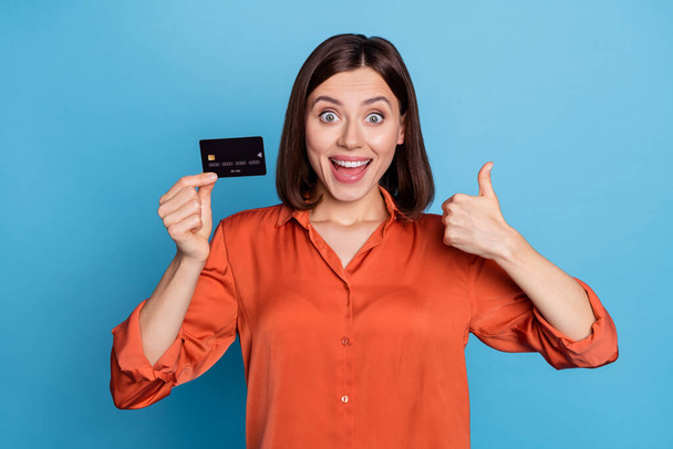 Portrait of attractive trendy cheerful girl holding in hand bank card showing thumbup isolated over bright blue color background. - Φωτογραφία, εικόνα