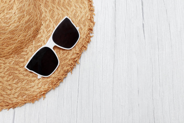 straw cap and sunglasses on a light wooden background - Foto, afbeelding