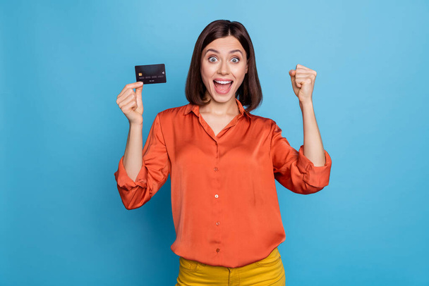 Portrait of attractive cheerful lucky girl holding in hand bank card nfc rejoicing isolated over bright blue color background. - Foto, afbeelding