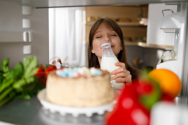 Girl sniffs milk from the bottle she took in the refrigerator - Valokuva, kuva