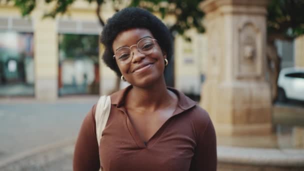 Femme africaine joyeuse portant des lunettes regardant charmante caméra à l'extérieur. Fille frisée insouciante souriant sincèrement à la caméra ayant une bonne humeur - Séquence, vidéo