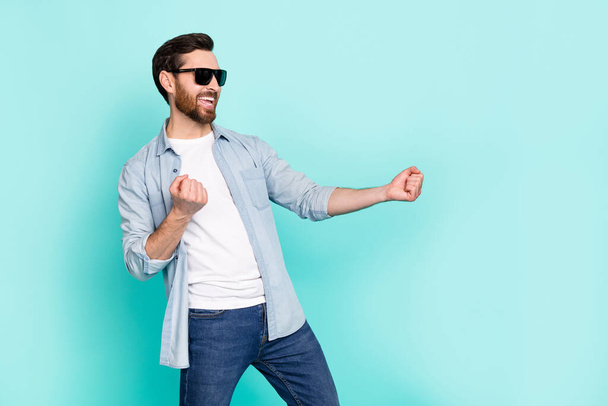 Photo of positive overjoyed guy have good mood raise fists enjoy dancing isolated on turquoise color background. - Photo, image