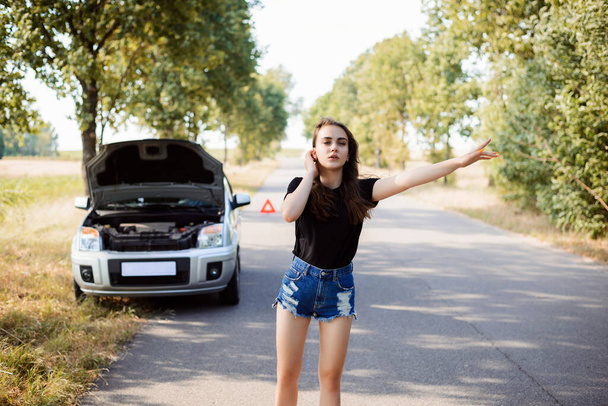 Attractive young student woman tries to stop passerby car and ask for a help because her car has broken - Photo, Image