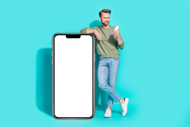 Photo of influencer blogger man hold telephone read message empty space wear pullover jeans isolated blue color background. - Foto, Imagen