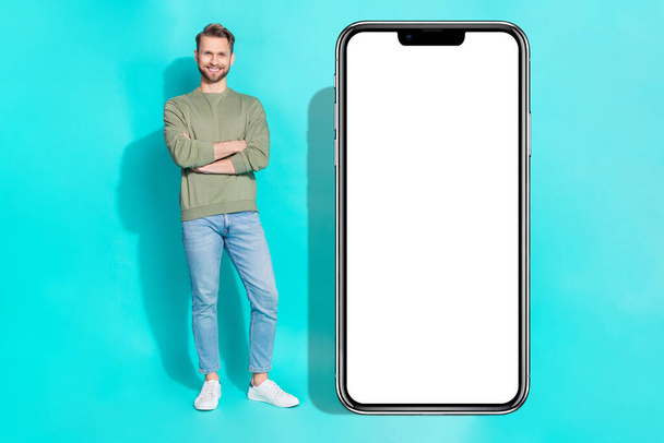 Full body photo of millennial guy crossed arms near telephone wear shirt jeans shoes isolated on turquoise background. - 写真・画像
