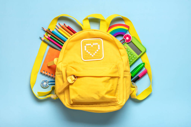 Back to school, education concept Yellow backpack with school supplies - notebook, pens, eraser rainbow, numbers isolated on blue background Top view Copy space Flat lay composition. - Photo, Image