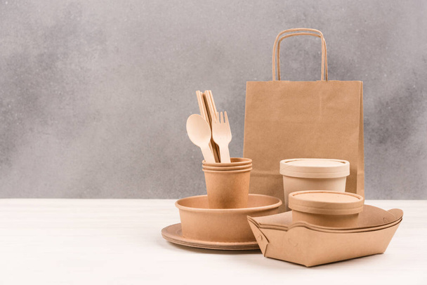 Paper utensils - paper plates, food containers, bag, cups and wooden cutlery set against gray wall background with copy space. Sustainable food packaging concept. Eco tableware  - Photo, Image