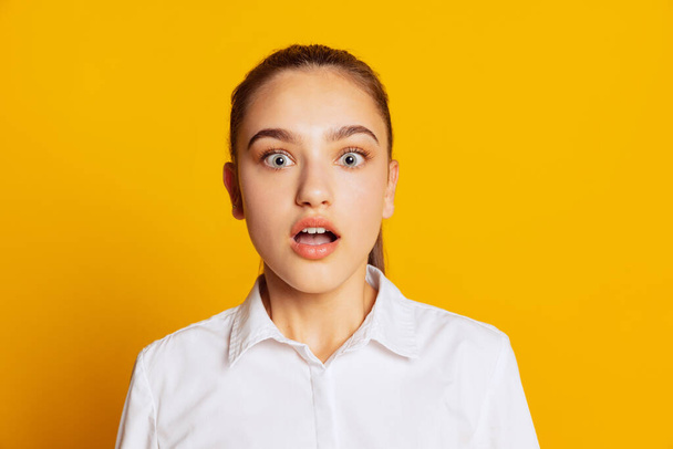 Shock news. Closeup portrait of surprised girl looking at camera with wide open eyes isolated on yellow background. Concept of beauty, art, fashion, youth, sales and ads. Student looks excited - Photo, image
