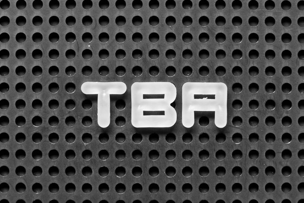 Λευκό αλφάβητο γράμμα στη λέξη TBA (σύντμηση του που πρέπει να ανακοινωθεί) σε μαύρο φόντο pegboard - Φωτογραφία, εικόνα