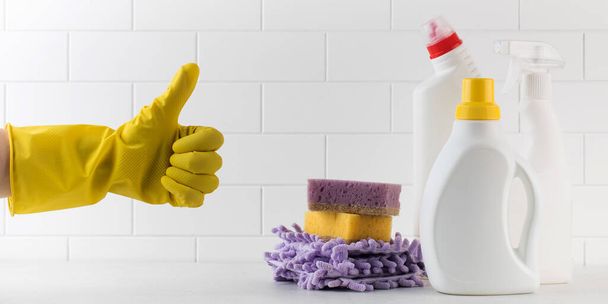  A set of different detergents, sponges and rags and a hand in a yellow glove shows a thumbs up on a light background. The concept of cleaning, hardware store, cleaning service. - Фото, изображение