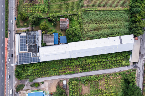 Luftaufnahme von Photovoltaik-Sonnenkollektoren oder Solarzellen auf dem Dach eines Fabrikgebäudes inmitten der Plantage auf dem Land. Alternative Energien, Nachhaltige Entwicklung, Erneuerbare Energien - Foto, Bild