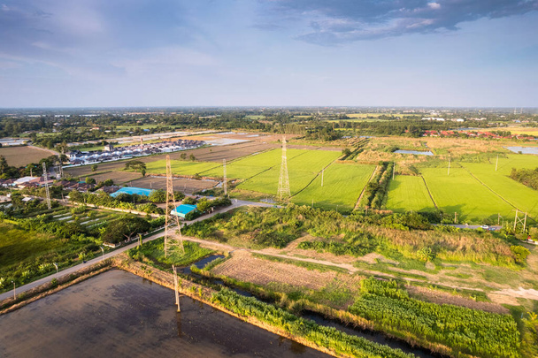 Vista aérea del poste de alto voltaje, torre de transmisión, pilón de electricidad, transmisión de energía eléctrica ubicada en el campo de arroz en el área remota de la comunidad - Foto, imagen