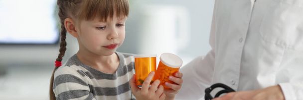 Portrait d'un enfant jouant avec des bouteilles pleines de médicaments lors d'un rendez-vous chez le médecin. Une femme médecin tient stéthoscope pour examen. Concept pédiatre - Photo, image