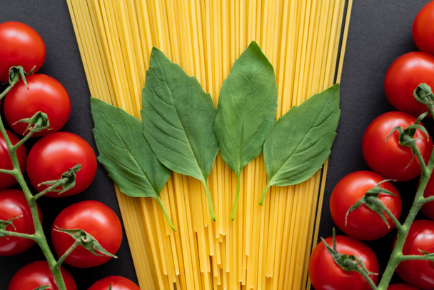 Vista superior de albahaca fresca sobre espaguetis cerca de tomates cherry sobre fondo negro  - Foto, imagen