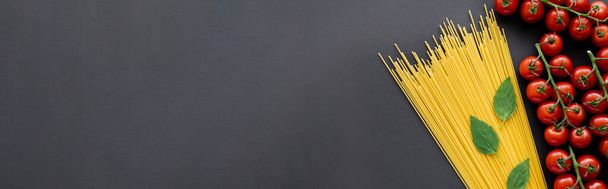 Κάτοψη του φυσικού βασιλικού και ντοματίνια κοντά σε ωμά ζυμαρικά σε μαύρο φόντο, banner  - Φωτογραφία, εικόνα