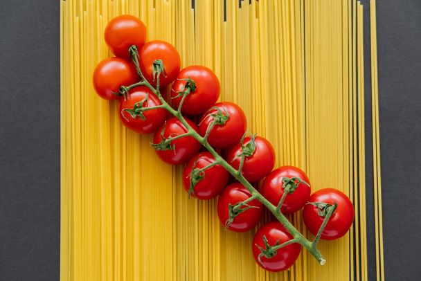 Top view of organic cherry tomatoes on raw pasta on black background  - Zdjęcie, obraz
