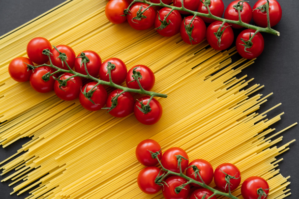 Top view of cherry tomatoes on branches on raw spaghetti on black background  - Photo, Image