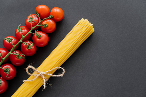 Top view of raw pasta and cherry tomatoes on black background  - Zdjęcie, obraz