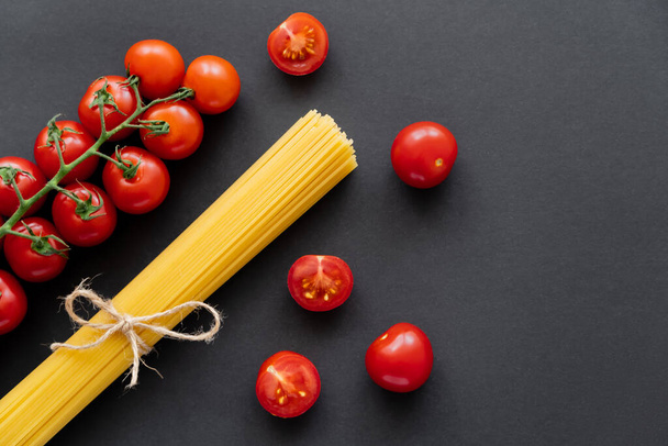 Top view of organic cherry tomatoes and raw spaghetti on black background  - Fotó, kép