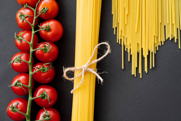 Top view of raw spaghetti and cherry tomatoes on black background  - Zdjęcie, obraz