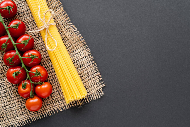 Top view of fresh cherry tomatoes and uncooked pasta on sackcloth on black background  - Fotó, kép