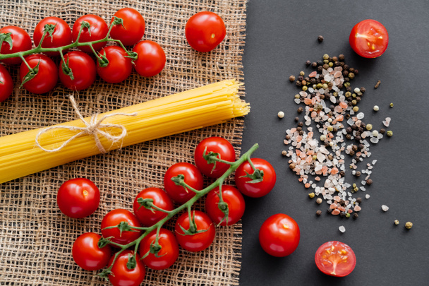 Baharatların yanındaki sebzelerin ve siyah arka plandaki çuval bezinin üzerindeki çiğ spagettinin üst görüntüsü.  - Fotoğraf, Görsel