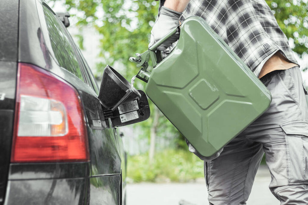 Egy férfi benzint önt egy tartályból egyenesen egy kocsi tartályába. Zöld Jerrycan tele benzinnel. Üzemanyaghiány utazás közben. - Fotó, kép