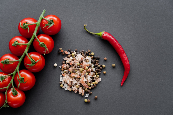 Horní pohled na cherry rajčata v blízkosti chilli paprika a koření na černém pozadí  - Fotografie, Obrázek