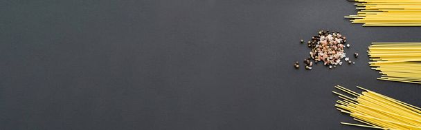 Widok z góry przyprawy i niegotowane makarony na czarnym tle, baner  - Zdjęcie, obraz