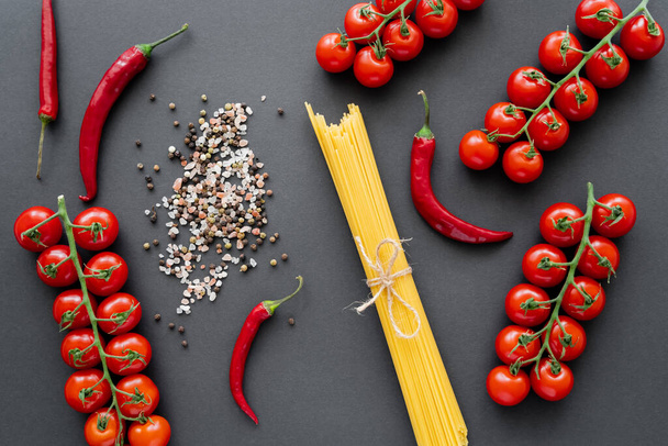 Top näkymä raaka pasta lähellä punaisia vihanneksia ja mausteita mustalla pohjalla  - Valokuva, kuva