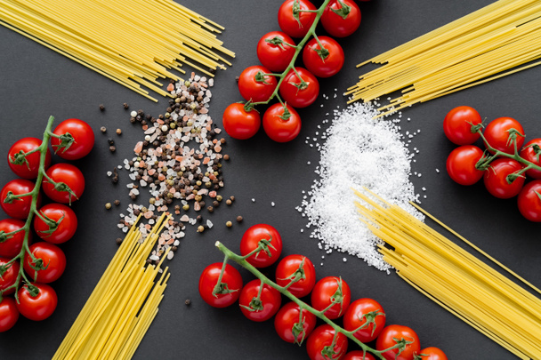 Flat lay with uncooked pasta near cherry tomatoes and salt on black background  - Photo, Image
