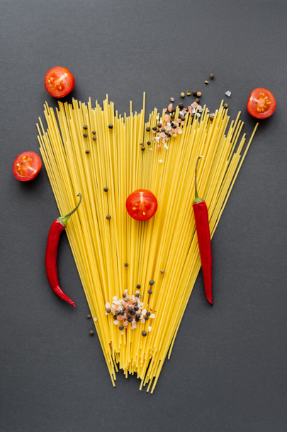 Flat lay with red vegetables and spices on spaghetti on black background  - Photo, Image