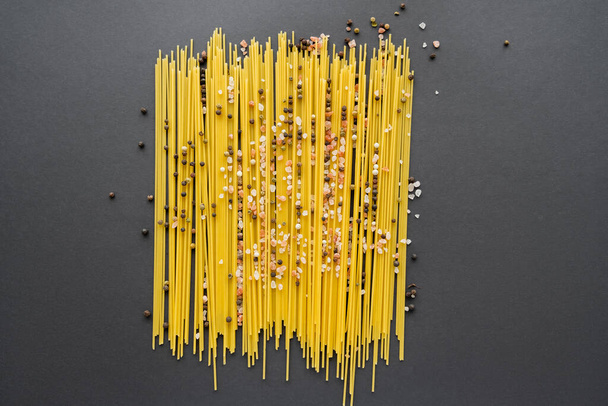 Draufsicht auf Gewürze und ungekochte Pasta auf schwarzem Hintergrund  - Foto, Bild