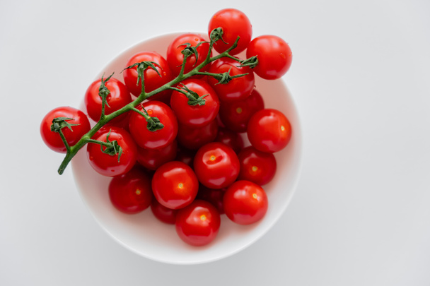 Vista superior de tomates cherry frescos en rama en tazón aislado en blanco  - Foto, imagen