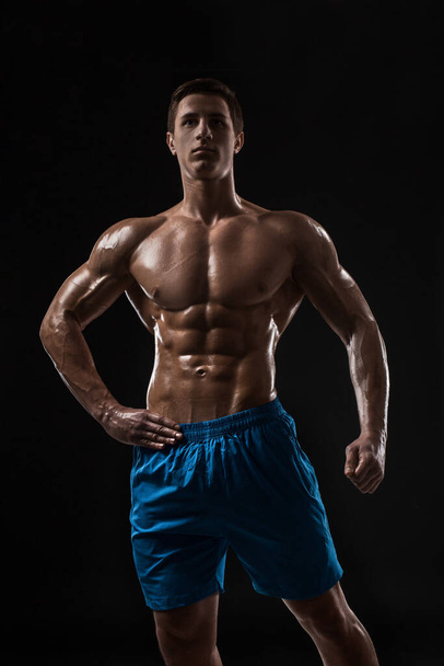 Muscular e ajuste jovem fisiculturista fitness modelo masculino posando sobre fundo preto. Estúdio tiro no fundo preto
. - Foto, Imagem