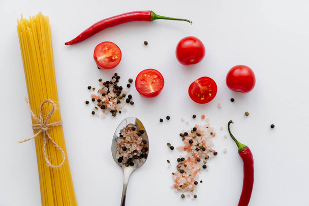 Horní pohled na syrové těstoviny v blízkosti koření s cherry rajčaty a chilli paprikou na bílém pozadí  - Fotografie, Obrázek