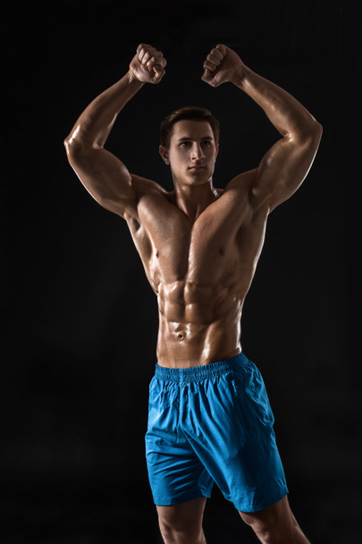 Muscular and fit young bodybuilder fitness male model posing over black background. Studio shot on black background. - 写真・画像