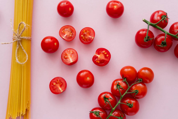 Top view of raw pasta and cherry tomatoes on pink surface - Φωτογραφία, εικόνα