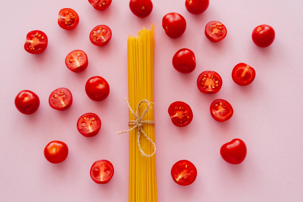 Flat lay of uncooked pasta and cherry tomatoes on pink surface - Photo, Image